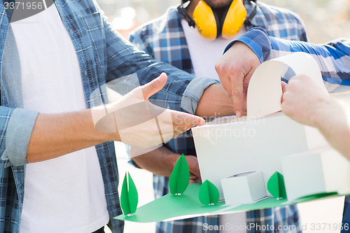 Image of close up of builders with paper house model