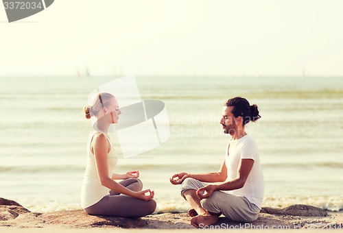 Image of smiling couple making yoga exercises outdoors