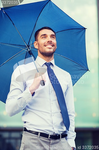 Image of young smiling businessman with umbrella outdoors