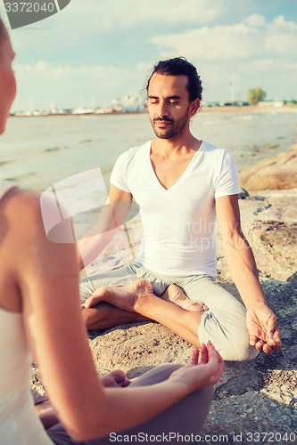 Image of smiling couple making yoga exercises outdoors