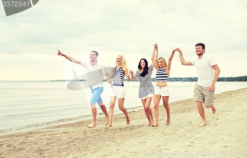 Image of smiling friends in sunglasses running on beach