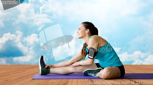 Image of smiling woman stretching leg on mat over clouds