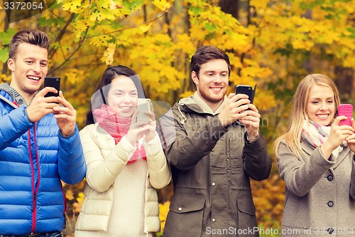 Image of smiling friends with smartphones in city park