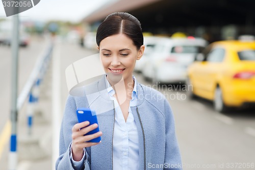 Image of smiling woman with smartphone over taxi in city