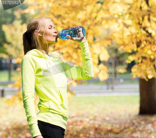 Image of woman drinking water after doing sports outdoors