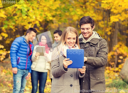 Image of group of smiling friends with tablets in park