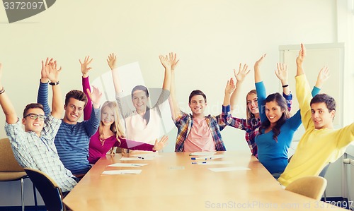 Image of group of smiling students raising hands in office
