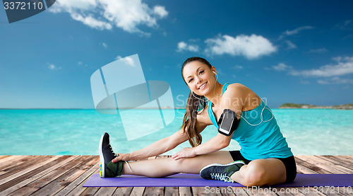 Image of smiling woman stretching leg on mat over sea