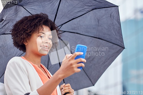 Image of businesswoman with umbrella texting on smartphone