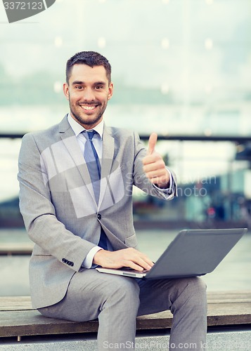 Image of smiling businessman working with laptop outdoors