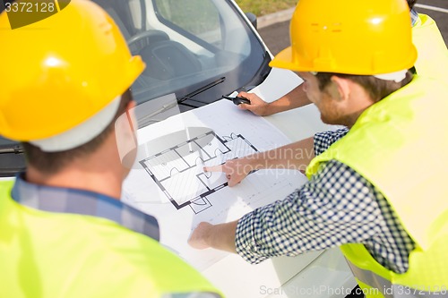 Image of close up of builders with blueprint on car hood