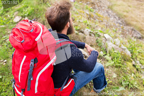 Image of man hiker with red backpack sitting on ground