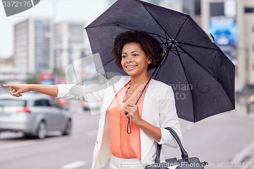 Image of happy african woman with umbrella catching taxi