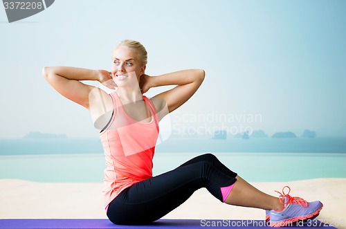 Image of smiling woman doing sit-up on mat over pool