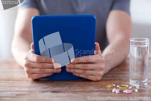 Image of close up of hands with tablet pc, pills and water