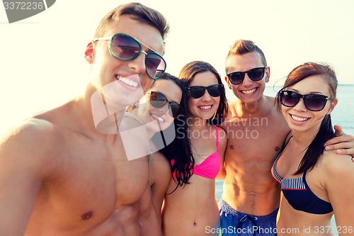 Image of group of smiling friends making selfie on beach