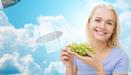 Image of happy woman eating grapes over sky