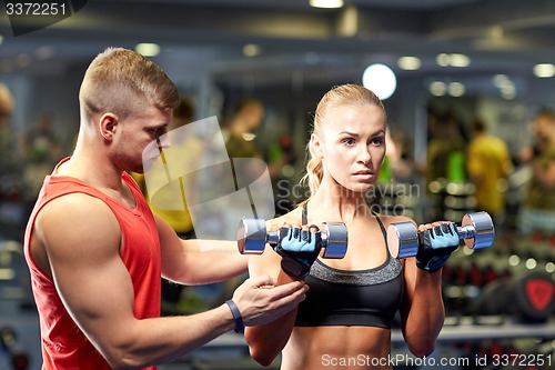 Image of young couple with dumbbells flexing muscles in gym