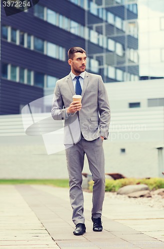 Image of young serious businessman with paper cup outdoors