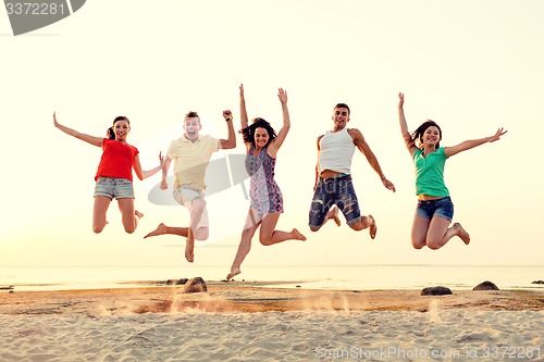 Image of smiling friends dancing and jumping on beach