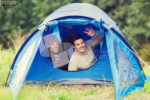Image of smiling couple of tourists looking out from tent