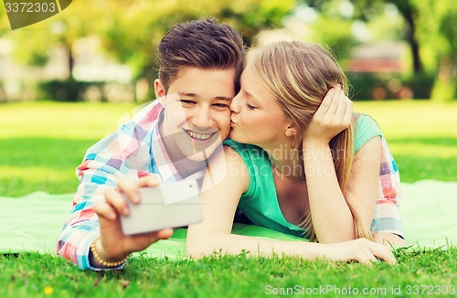 Image of smiling couple making selfie and kissing in park