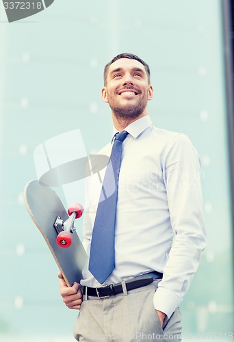 Image of young smiling businessman with skateboard outdoors