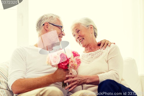 Image of happy senior couple with bunch of flowers at home
