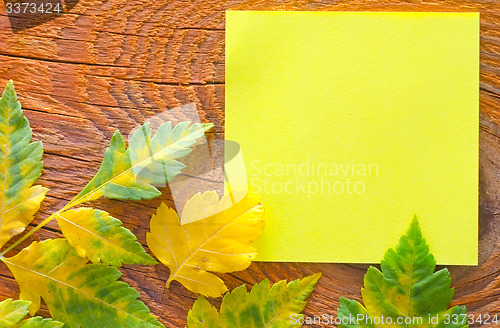 Image of note and leaves on wooden background