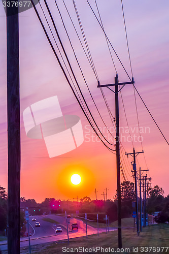Image of silhouetted electric pylon with power line at sunset