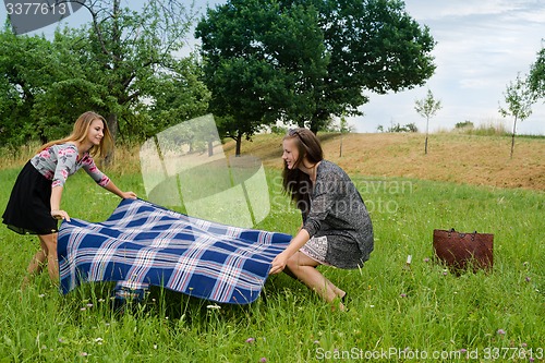 Image of Two girls  spreading a blanket for picnic