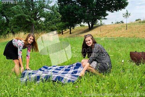 Image of Two girls  spreading a blanket for picnic