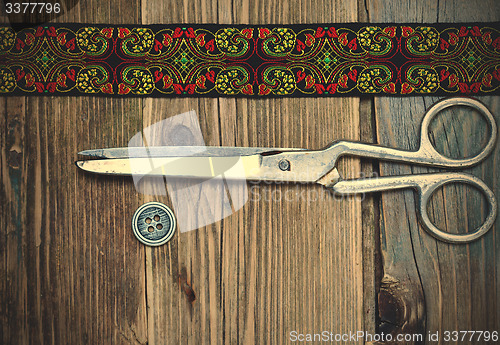 Image of vintage button, emroidered band and a tailor scissors