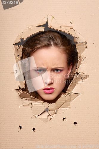 Image of Displeased woman peeping through hole in paper