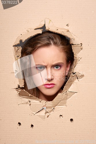 Image of Displeased girl peeping through hole in paper