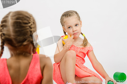 Image of Girl misunderstanding looks at her sister while playing with toys