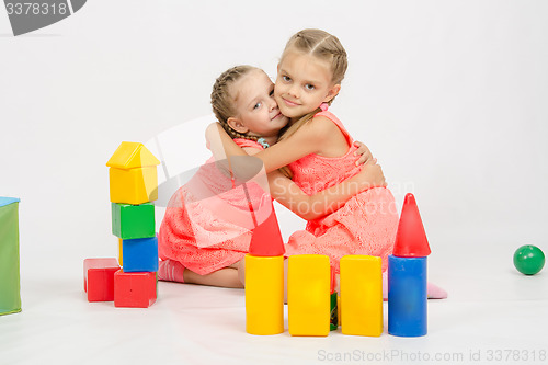 Image of Happy two girls embrace building a castle out of blocks