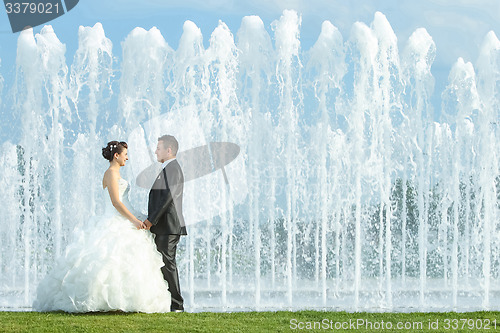 Image of Bride and groom holding hands in front of water fountain