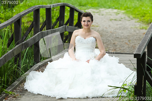 Image of Bride sitting on wooden bridge