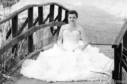 Image of Bride sitting on wooden bridge black and white