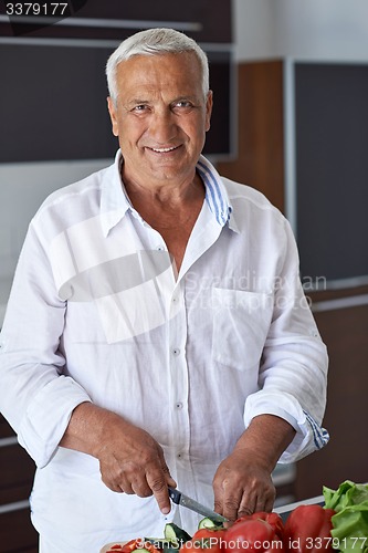 Image of senior man cooking at home preparing salad in kitchen