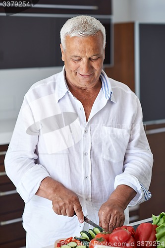 Image of senior man cooking at home preparing salad in kitchen