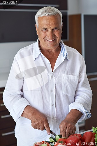 Image of senior man cooking at home preparing salad in kitchen