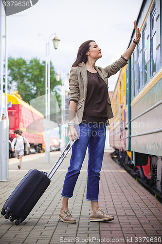 Image of woman with luggage waves his hand near passenger railcar 