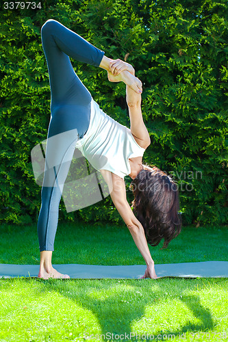 Image of beautiful woman doing yoga on a green grass