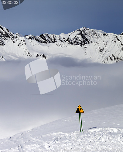 Image of Warning sing on ski slope and mountains in fog