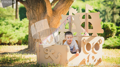 Image of Boy playing in cardboard boat at park.