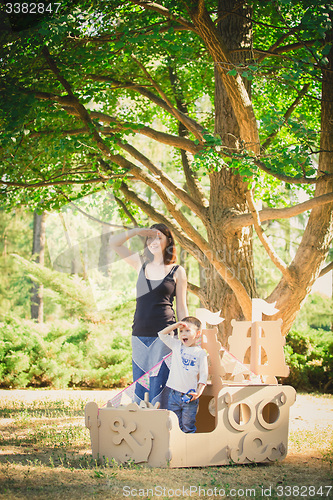 Image of Mom and child playing in a cardboard boat. Summer day.