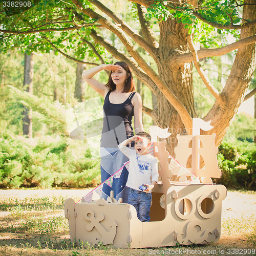 Image of Mom and child playing in a cardboard boat. Summer day.