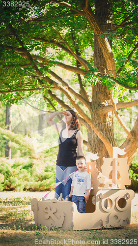 Image of Mom and child playing in a cardboard boat. Summer day.